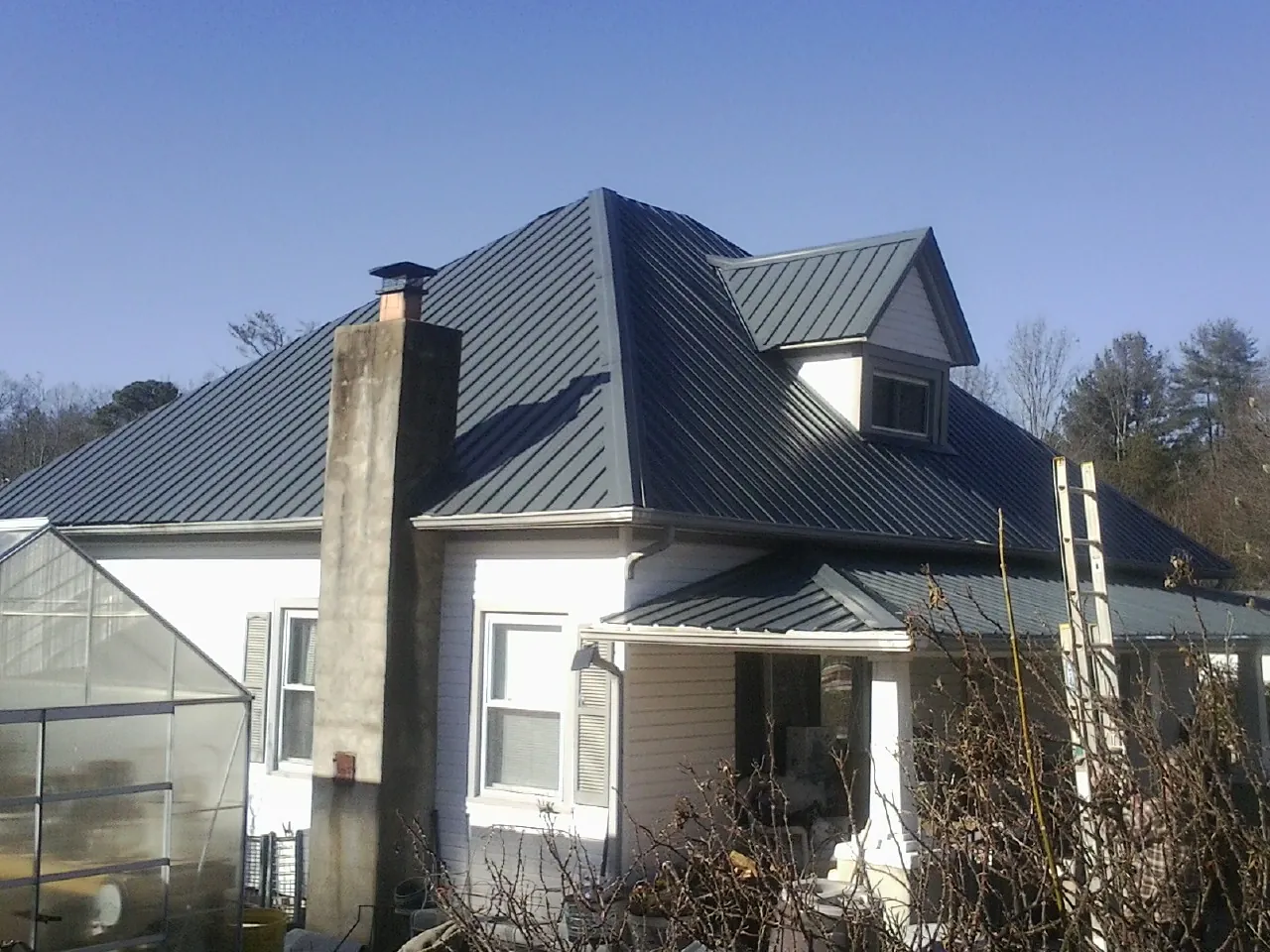 Dark blue standing seam metal roof on a white farmhouse with dormer — Slate & Tile Roof Repair by Roofing Brothers in Hollsopple
