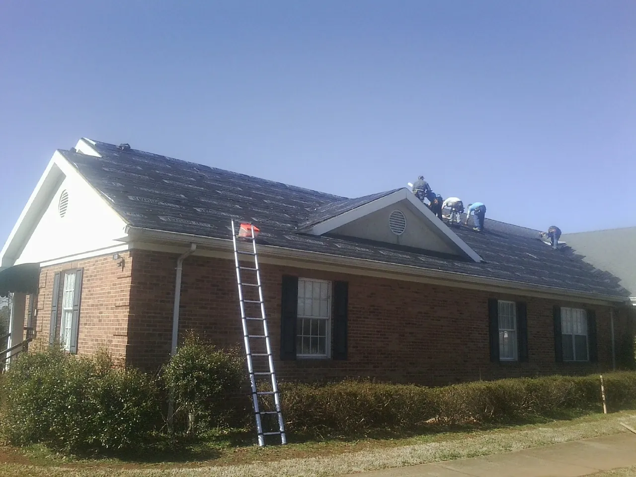 Crew tearing shingles off a brick ranch roof with a ladder set — Metal Roof Repair work by our crew in Hollsopple