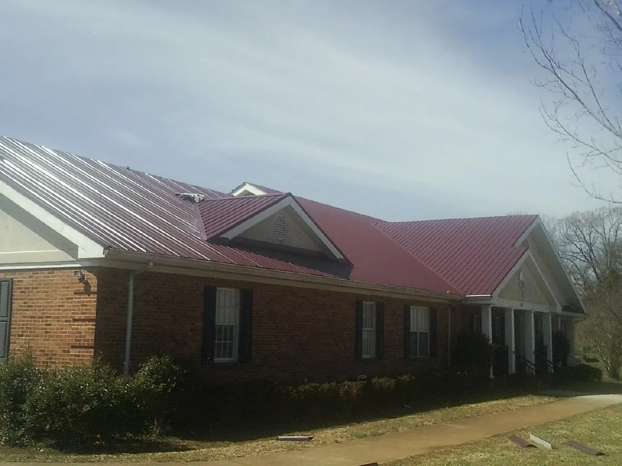 Red metal roof with gabled entries on a long brick building, from a Hail Damage Roof Repair job in Hollsopple