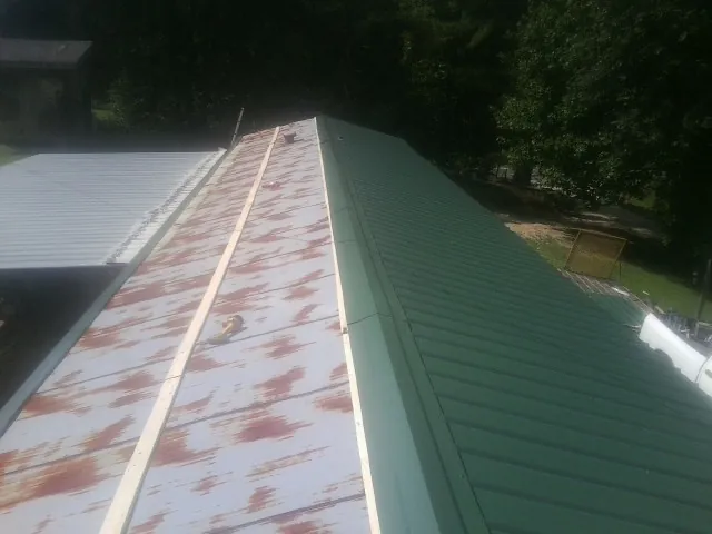 Old rusted panels beside newly installed green metal roofing — Wind Damage Roof Repair by Roofing Brothers in Hollsopple