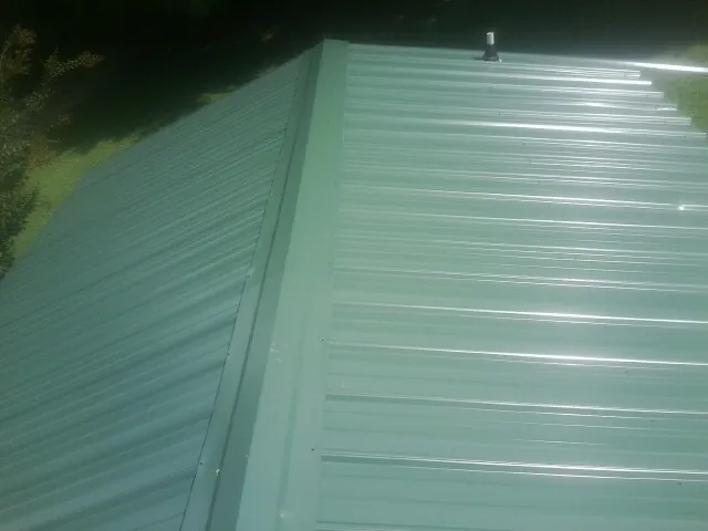 New green metal panels meeting at the ridge of a roof — Flat Roof Repair work by our crew in Hollsopple