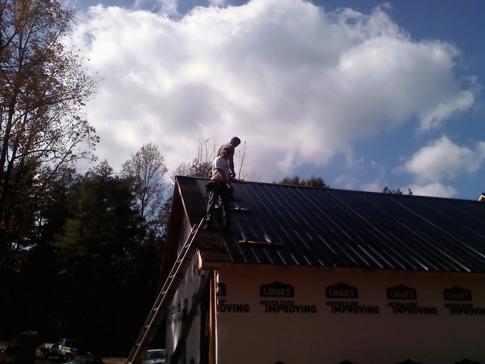 Roofer fastening dark metal panels high against a cloudy sky, from a Roof Inspection job in Hollsopple