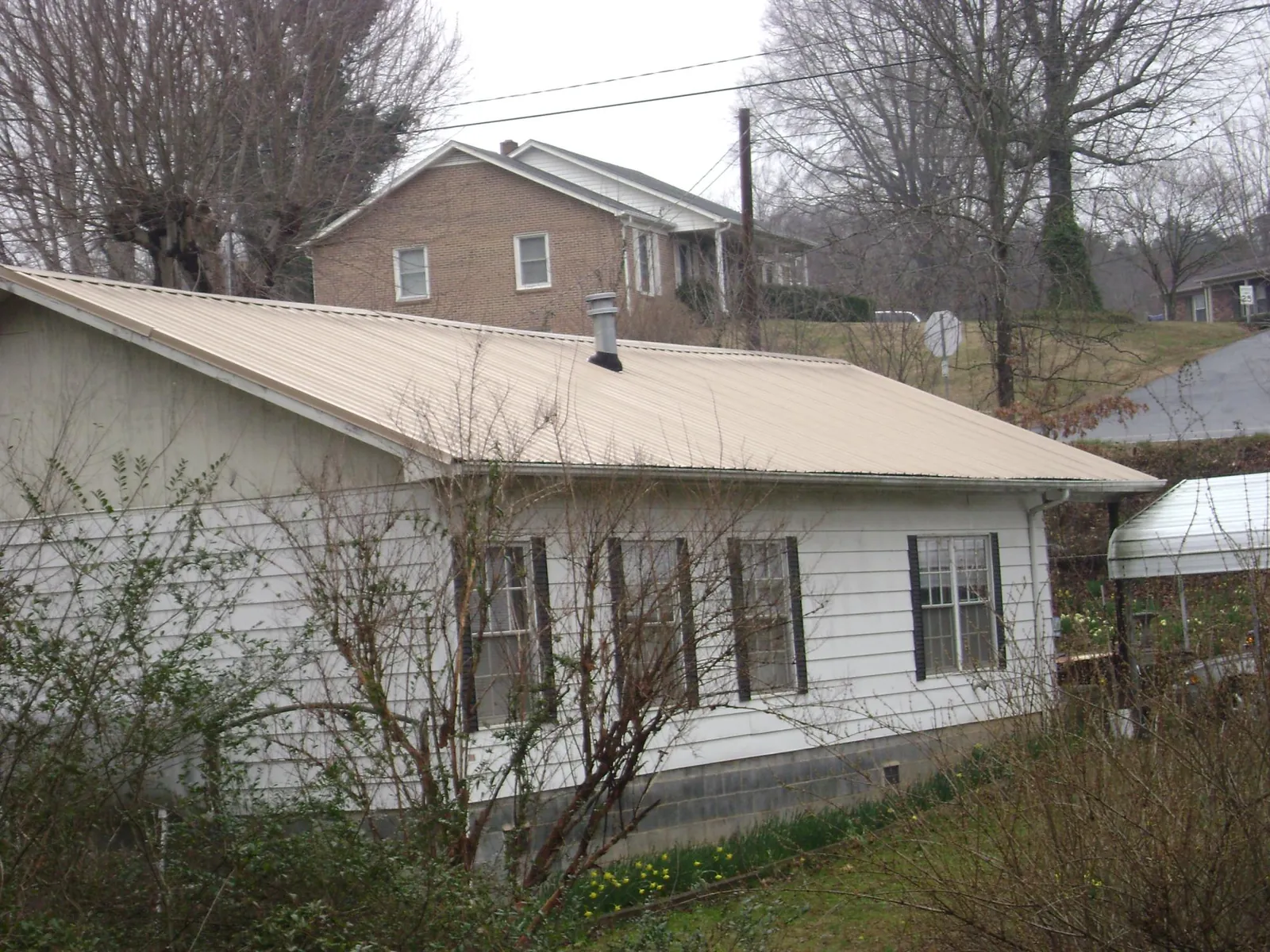 Tan metal roof on a white sided house set into a hillside — Commercial Roofing by Roofing Brothers in Hollsopple