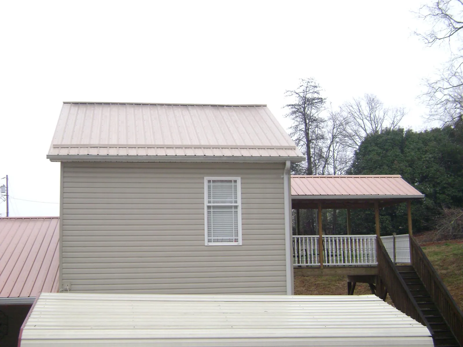 Tan metal roofs on a two story addition and attached porch, from a Roof Replacement job in Hollsopple